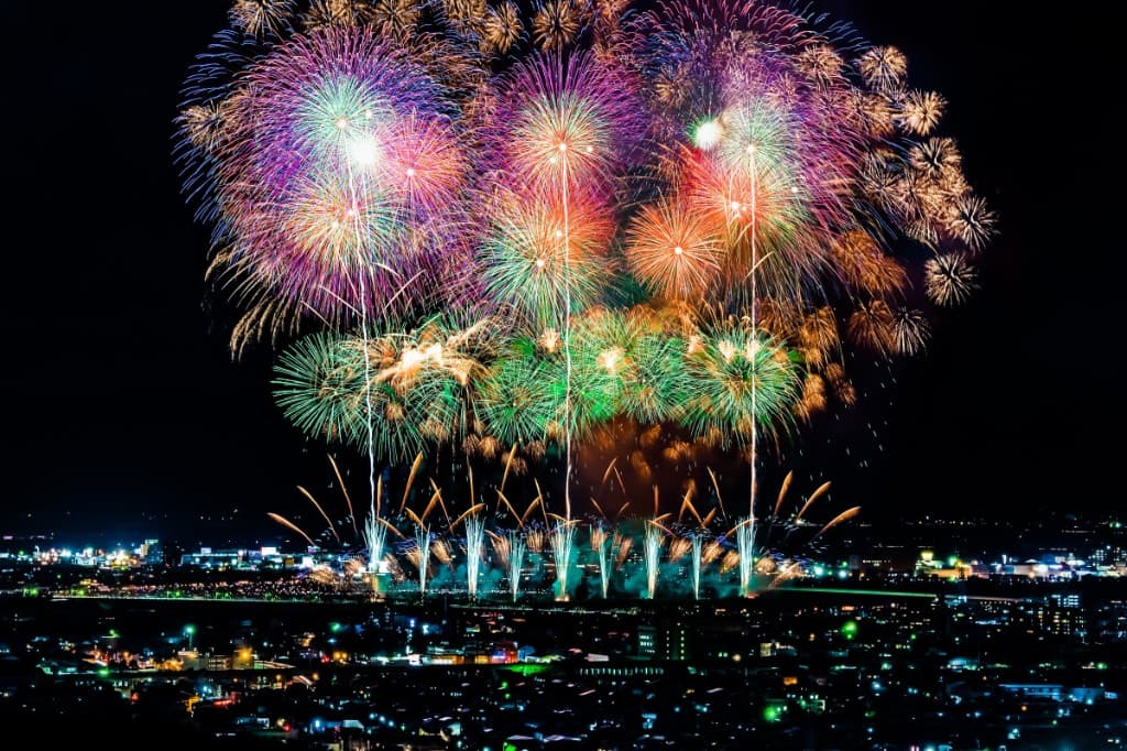 Massive multi-colored Nagaoka fireworks bursting over the city skyline at night