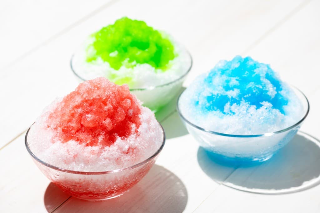 Three bowls of Japanese kakigori shaved ice in strawberry, melon, and blue Hawaii flavors
