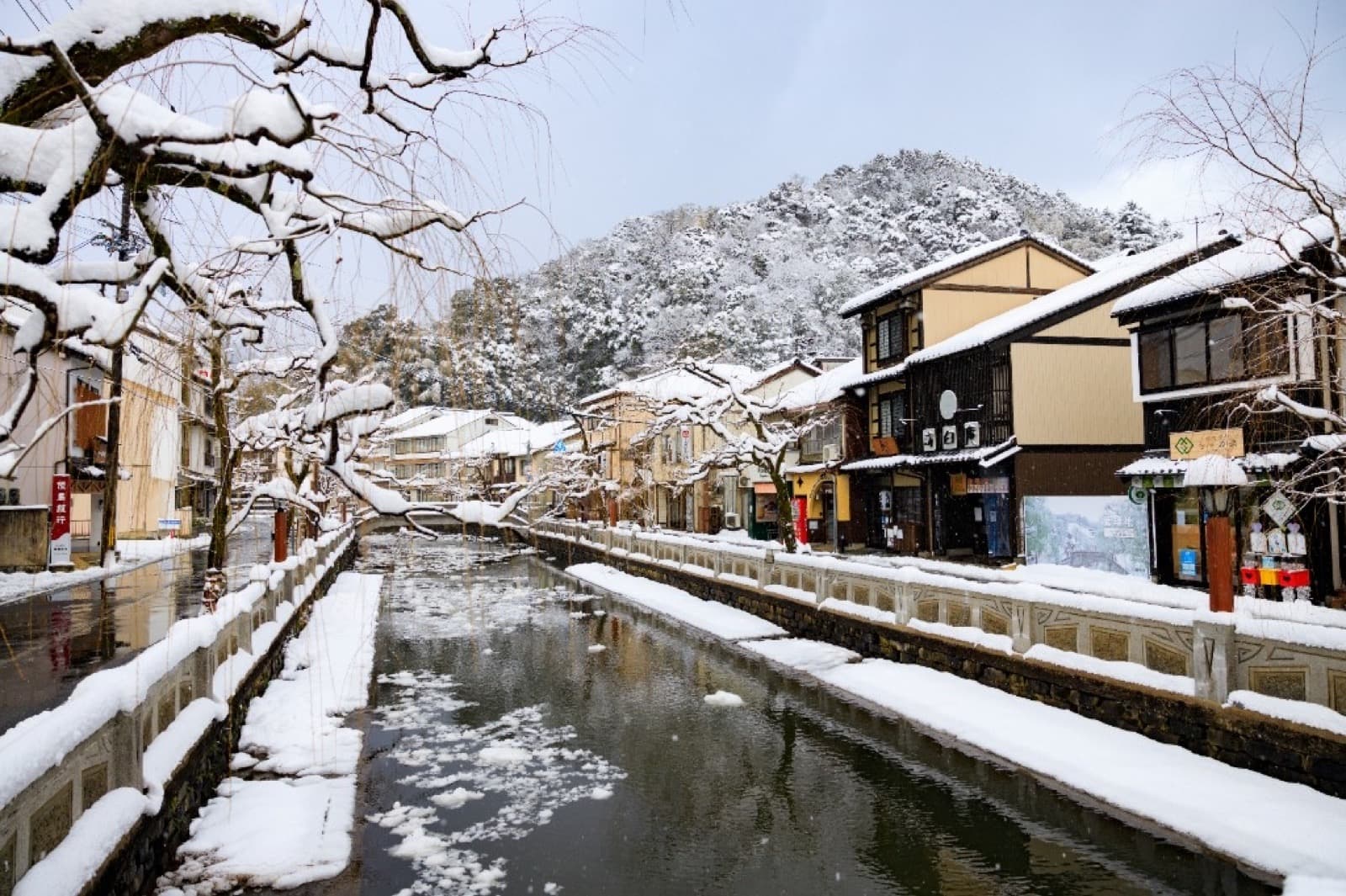 A snow-covered canal lined with traditional Japanese buildings in a winter onsen town