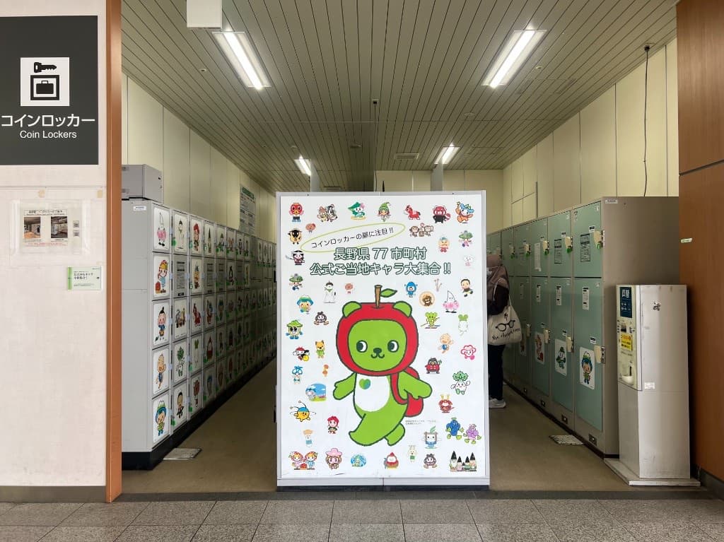 Rows of coin lockers at Nagano Station under a Coin Lockers sign, decorated with local mascot characters