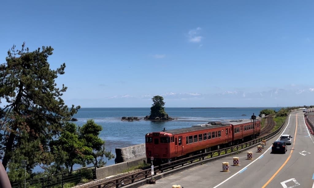 JR Himi Line train running along the Amaharashi Coast in Toyama, with the Tateyama Mountains across the bay