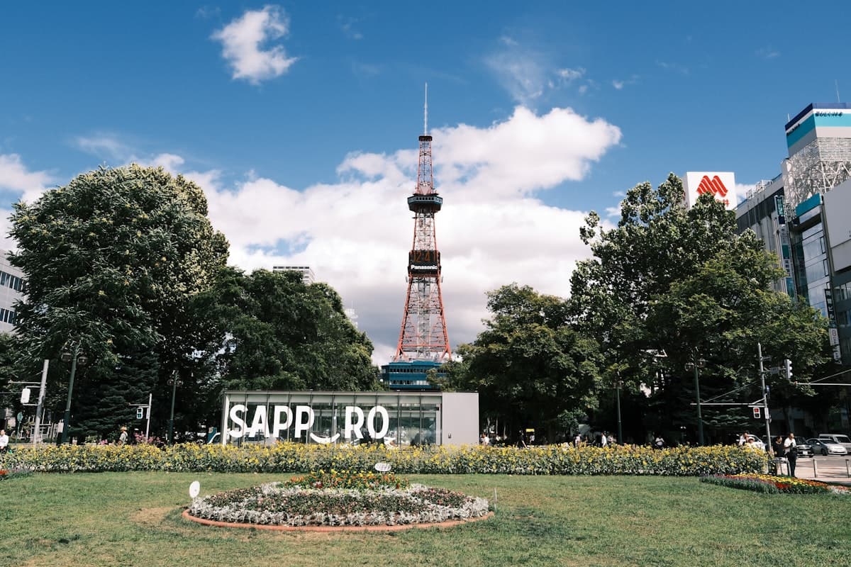 Der Fernsehturm von Sapporo auf Hokkaido unter klarem Sommerhimmel, mit grünen Bäumen im Odori-Park