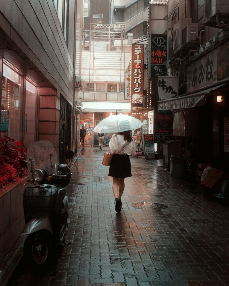 Eine Frau geht in Tokio bei leichtem Regen mit Schirm eine Straße entlang