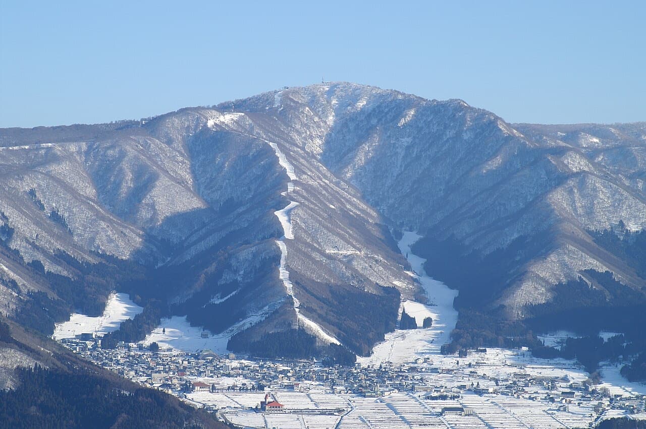 Nozawa Onsen village spread below snowy mountains with ski runs cut through the forest