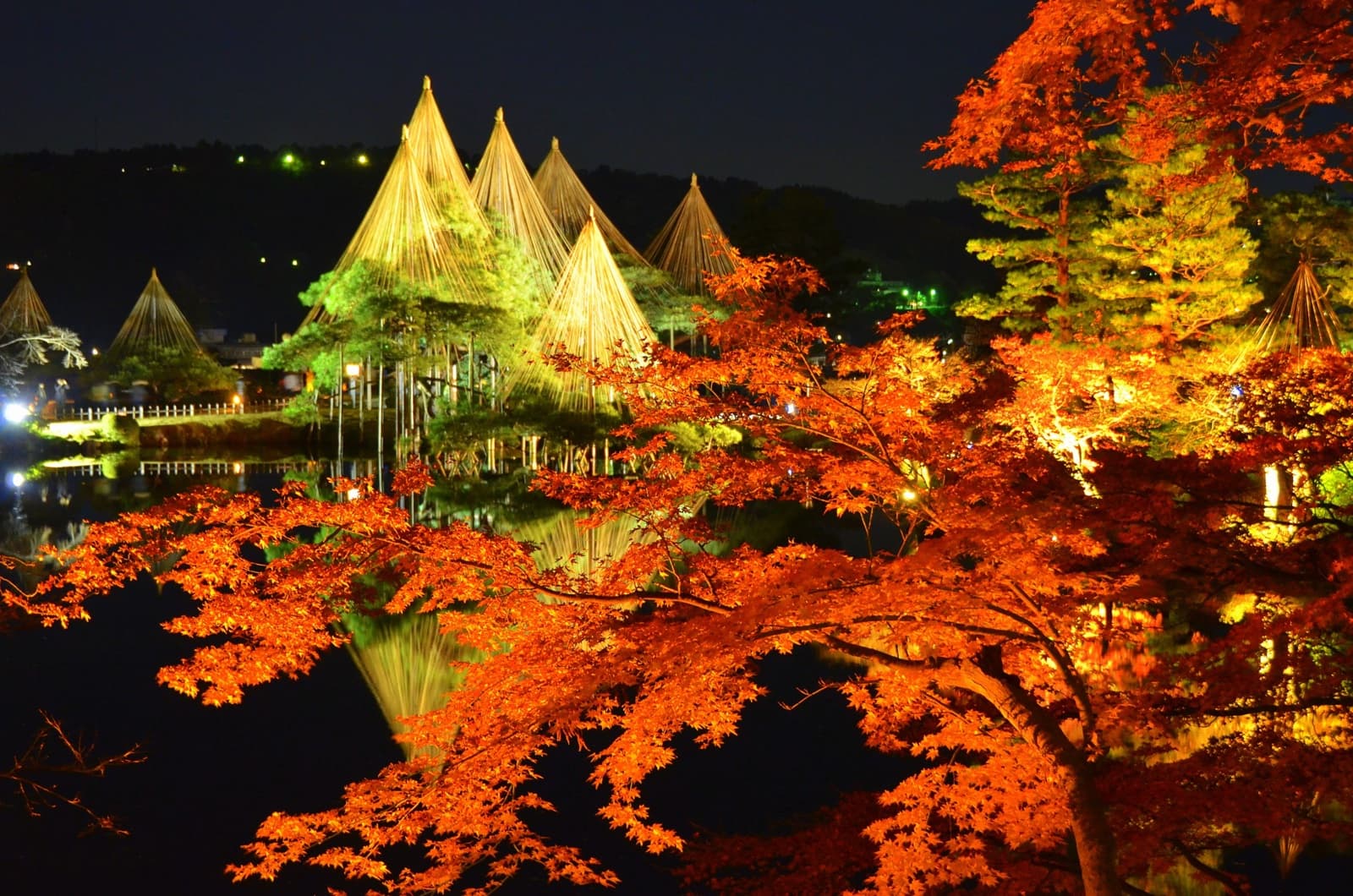 Kenrokuen at night in autumn — illuminated yukitsuri rope cones and red maples reflected in Kasumigaike Pond