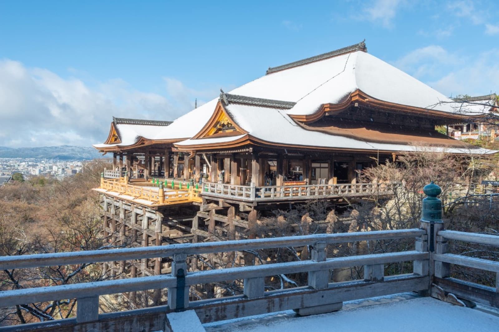 Kiyomizu-dera with snow on its roofs and railings under a bright blue winter sky, Kyoto city in the background