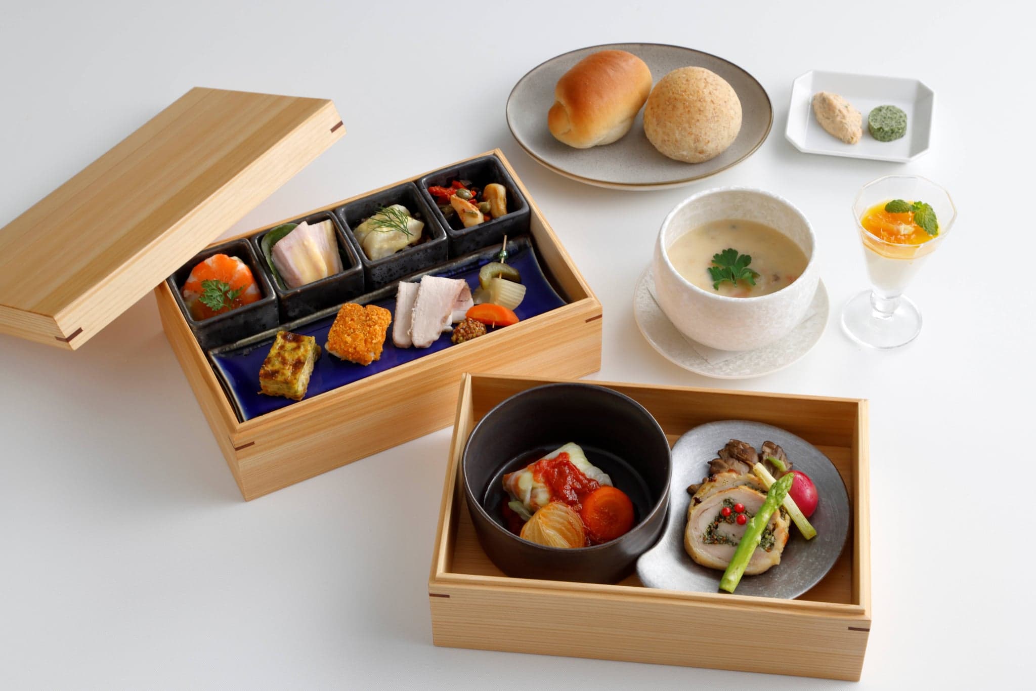 The French Zen set of Les Saveurs Shima: two wooden boxes holding small French dishes, with bread rolls, a cup of soup and a glass of orange dessert