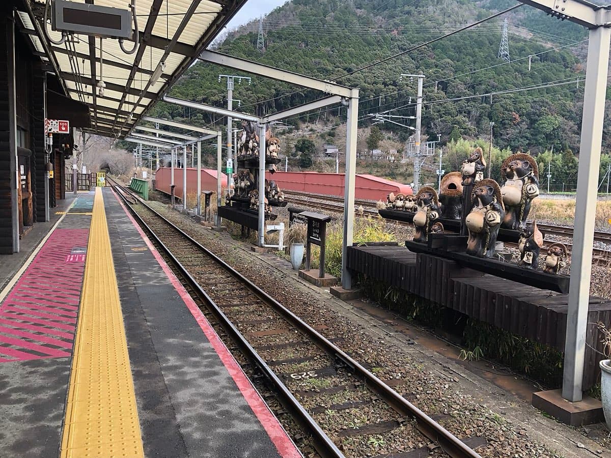 The platform at Torokko Kameoka Station with a yellow tactile strip, a covered roof and ceramic raccoon-dog statues beside the track