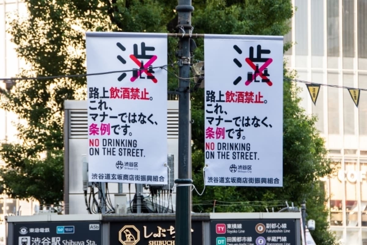 Street banner near Shibuya Station reading no drinking on the street — a ward ordinance, not just manners
