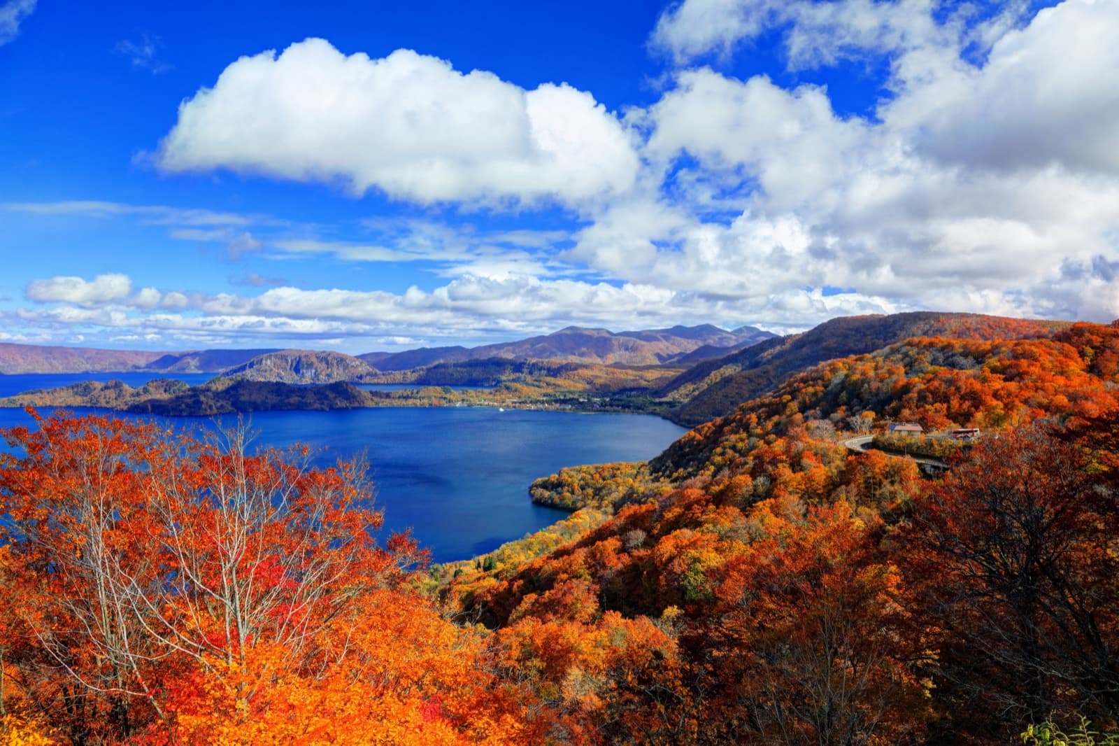 Deep blue caldera lake ringed by red and gold autumn forest under a bright sky