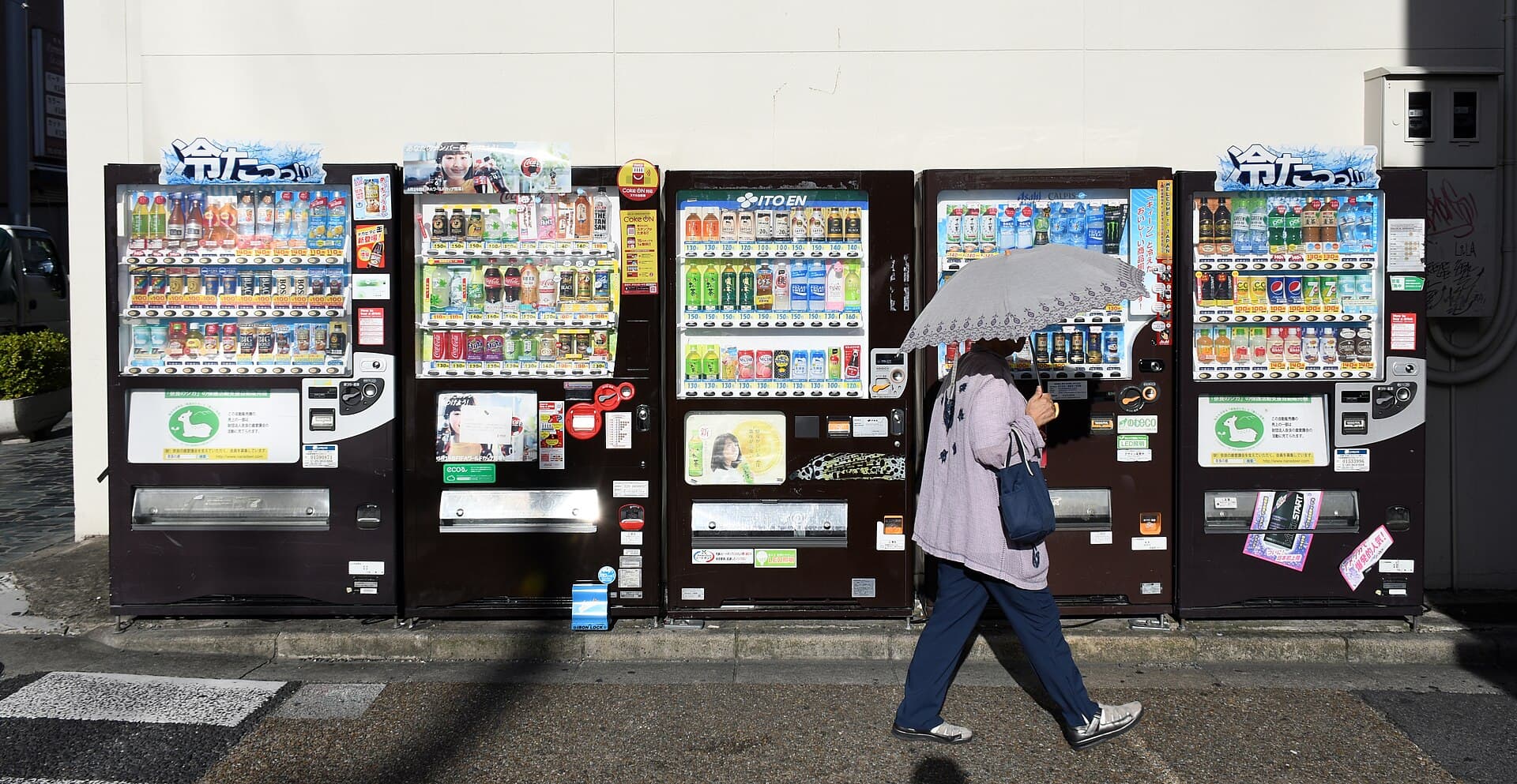 A row of Japanese street drink vending machines with recycling bins alongside