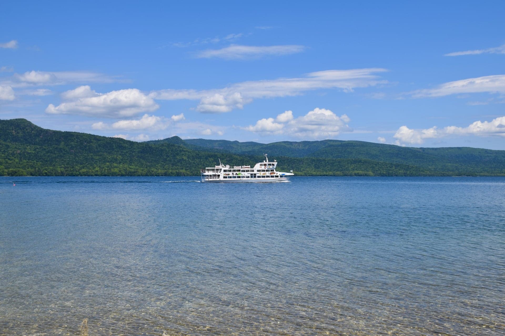 Sightseeing boat on Lake Akan, Hokkaido, with forested hills behind