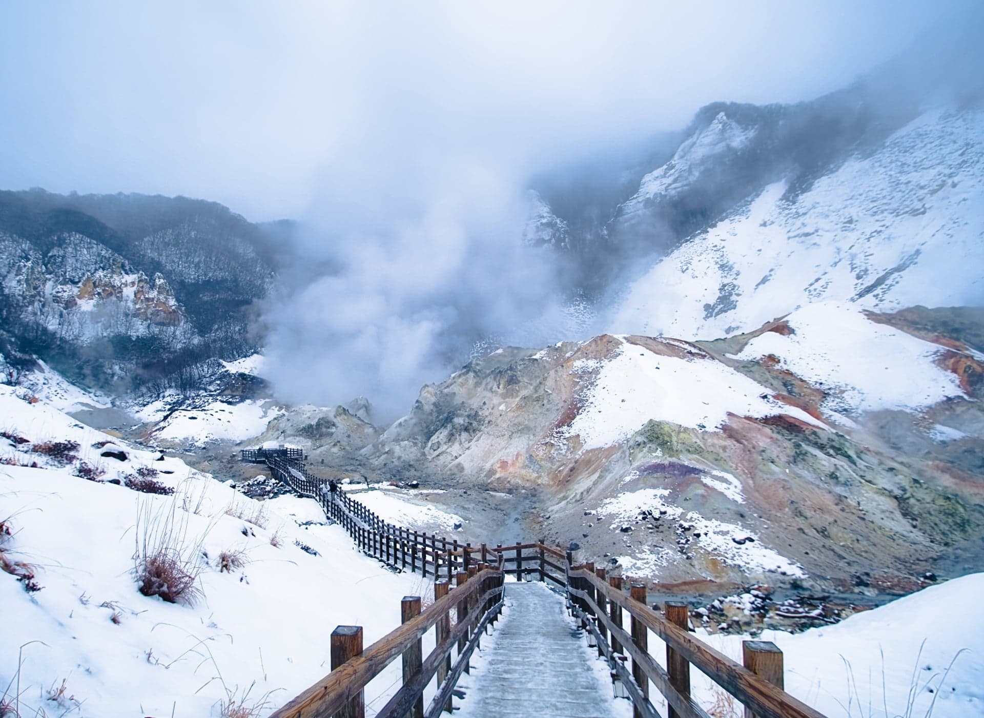 Steam rising from the snow-covered volcanic crater of Jigokudani in Noboribetsu, with a wooden boardwalk