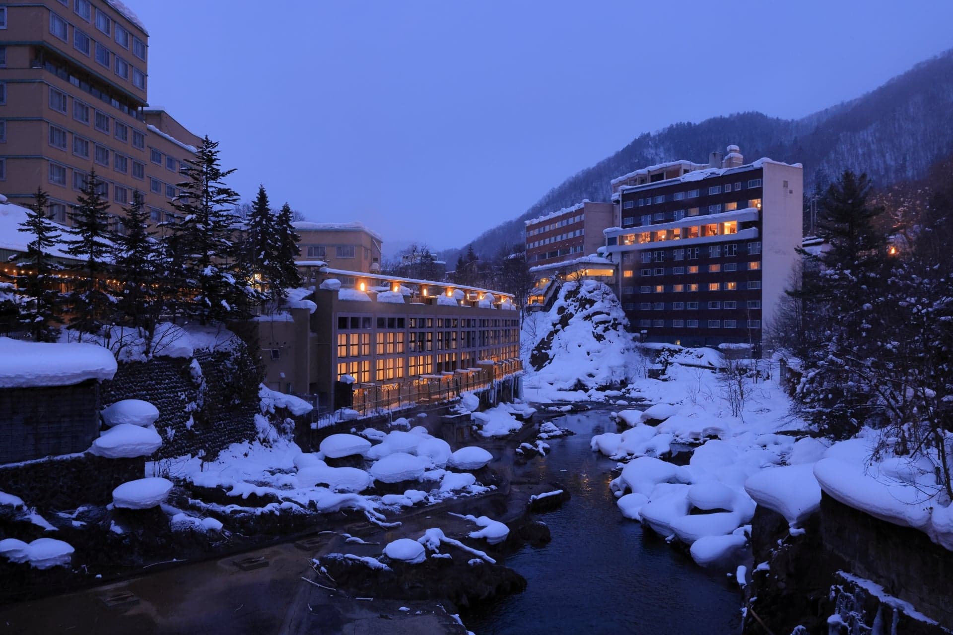 Jozankei Onsen at dusk, with snow-covered rocks in the river and hotels along the gorge