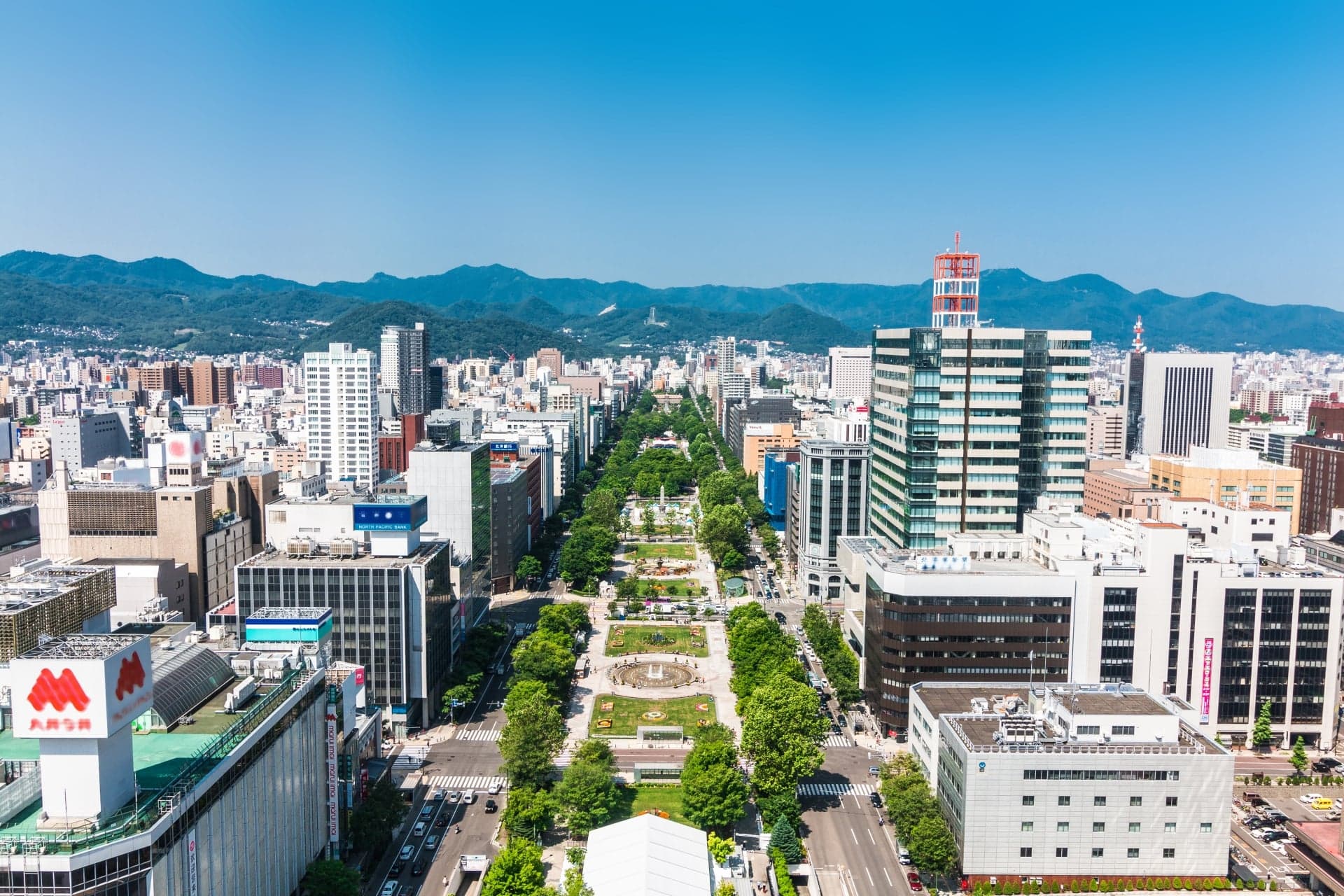 Odori Park seen from above as a long green strip running through central Sapporo, with mountains behind the city
