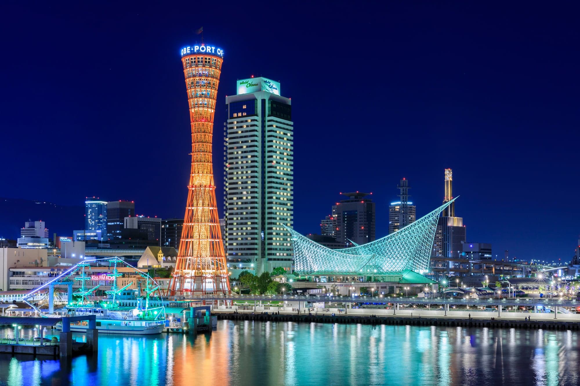 Kobe Port Tower lit red beside the white lattice of the Maritime Museum, reflected in the harbor at night