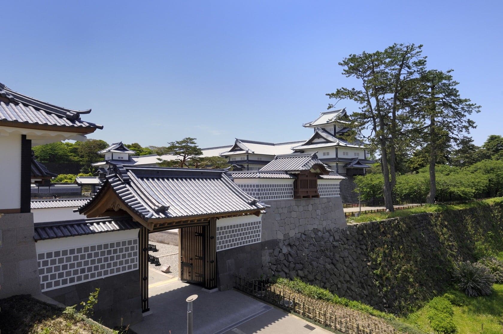 A white-walled turret and gate of Kanazawa Castle above tall stone walls under a clear sky