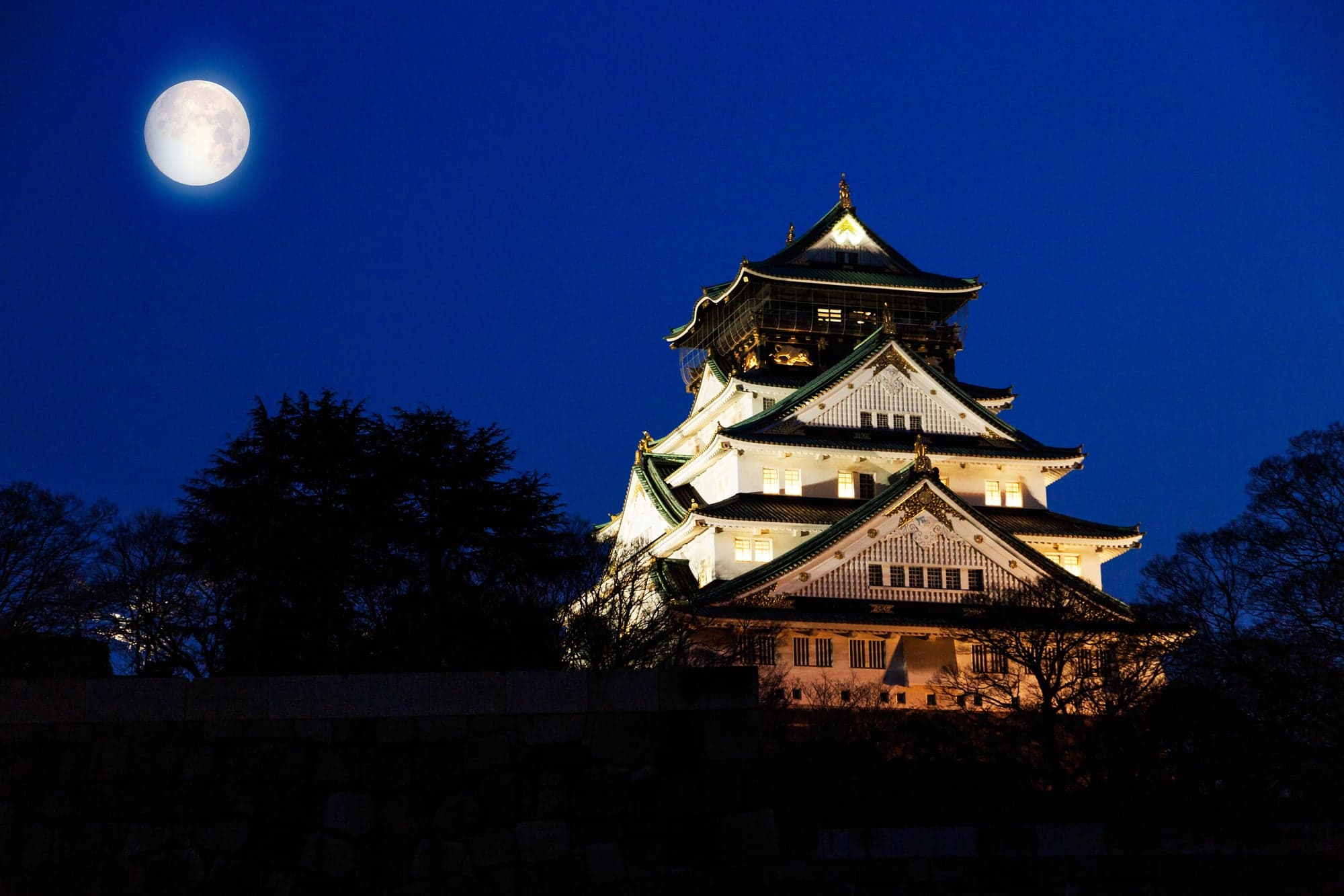 Osaka Castle keep lit up at night under a full moon