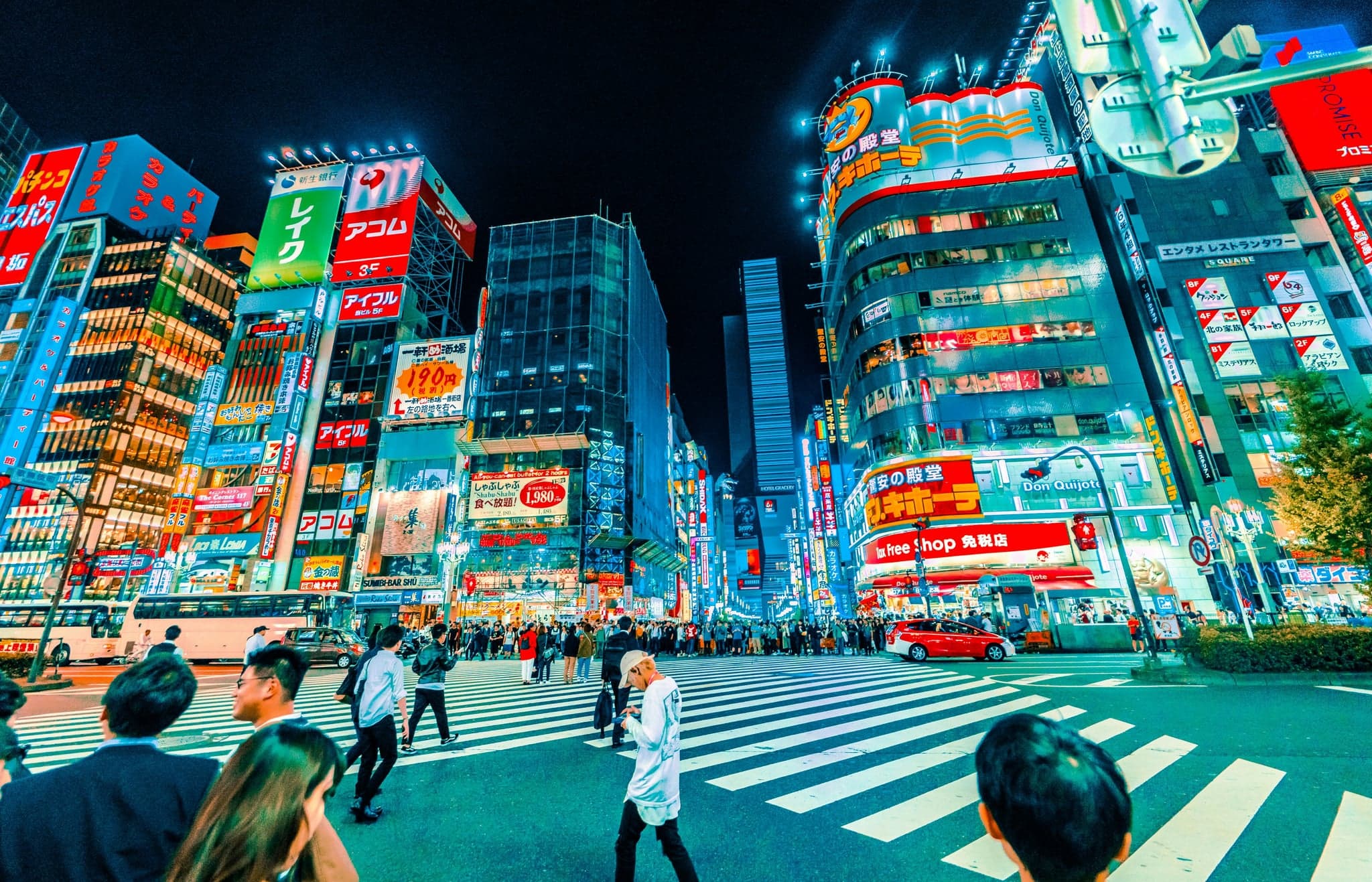 People crossing a street in Shinjuku at night under tall buildings covered in neon signs