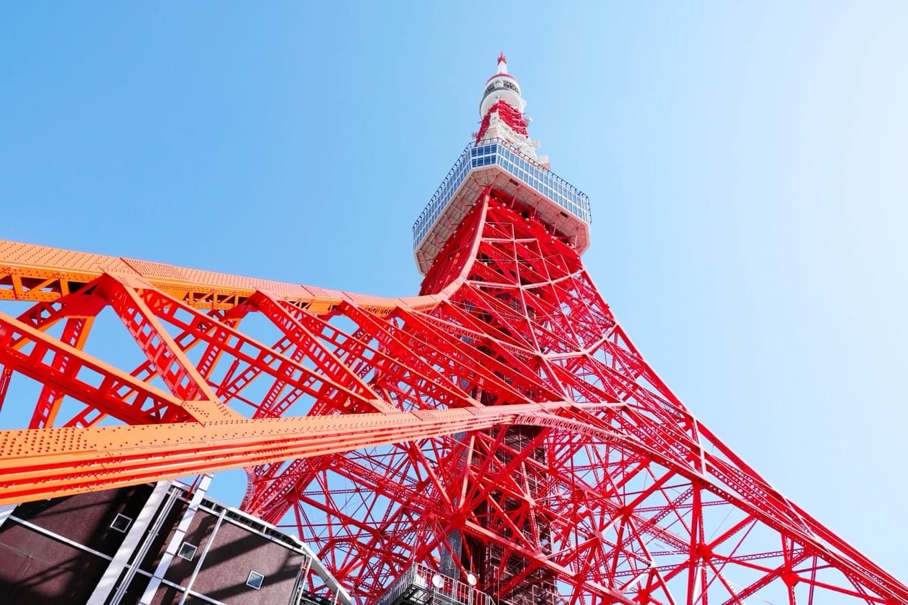 Looking up at the red and white steel lattice of Tokyo Tower against a blue sky