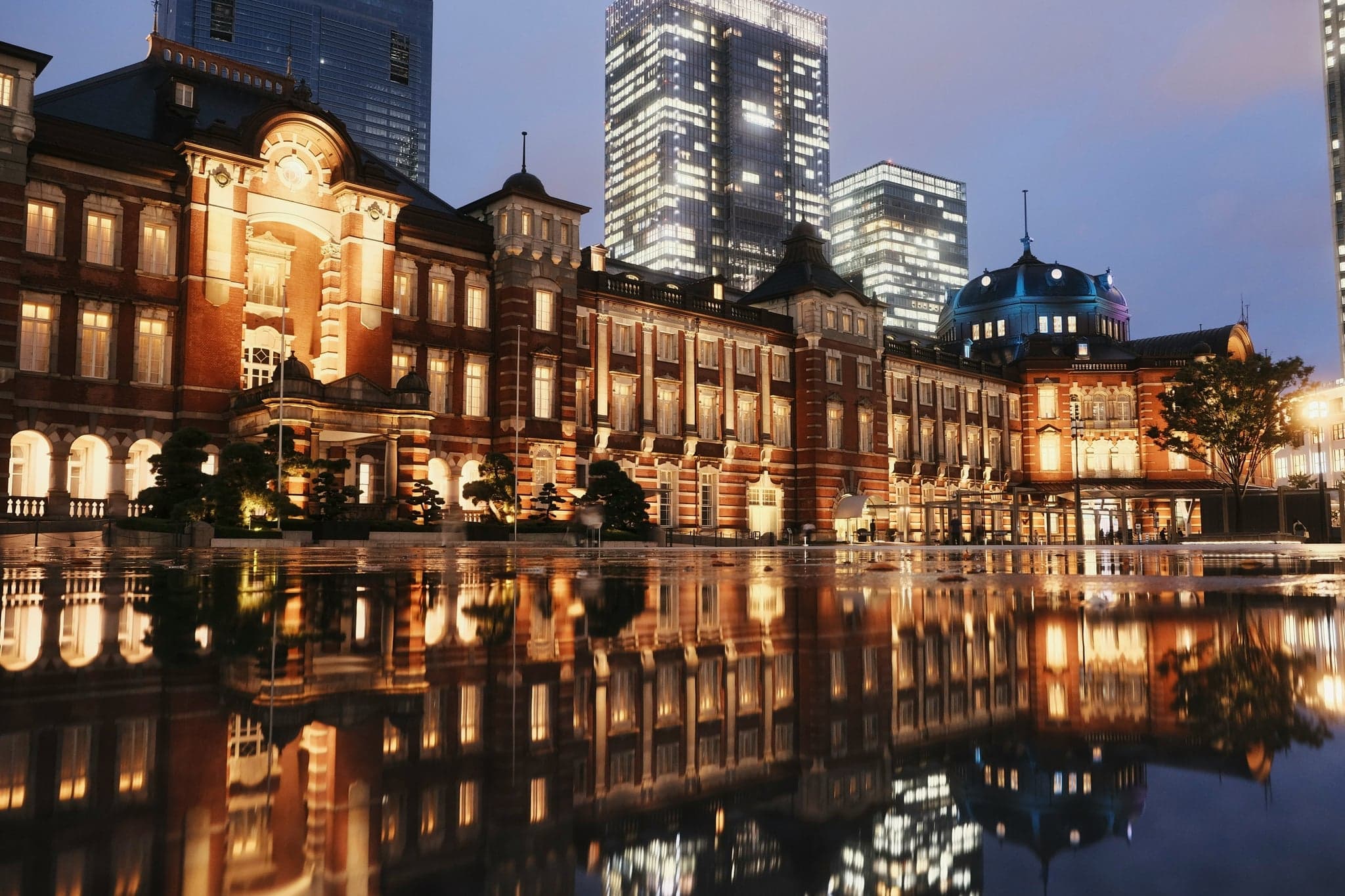 Tokyo Station's red-brick Marunouchi building lit at night and reflected in a wet plaza