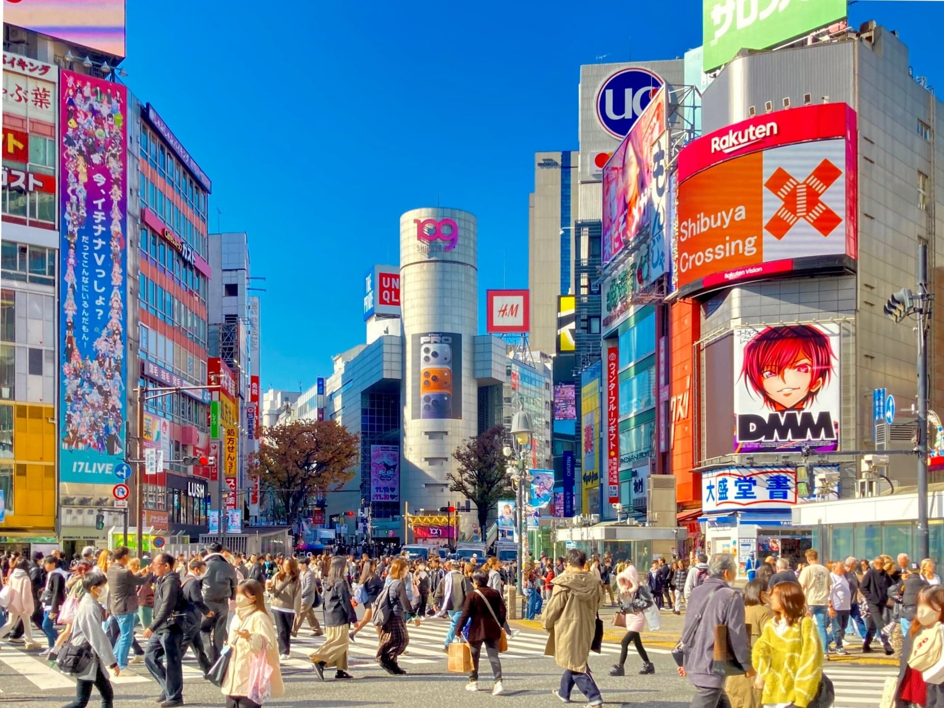 Hundreds of people crossing the Shibuya Scramble Crossing in daylight under giant advertising screens