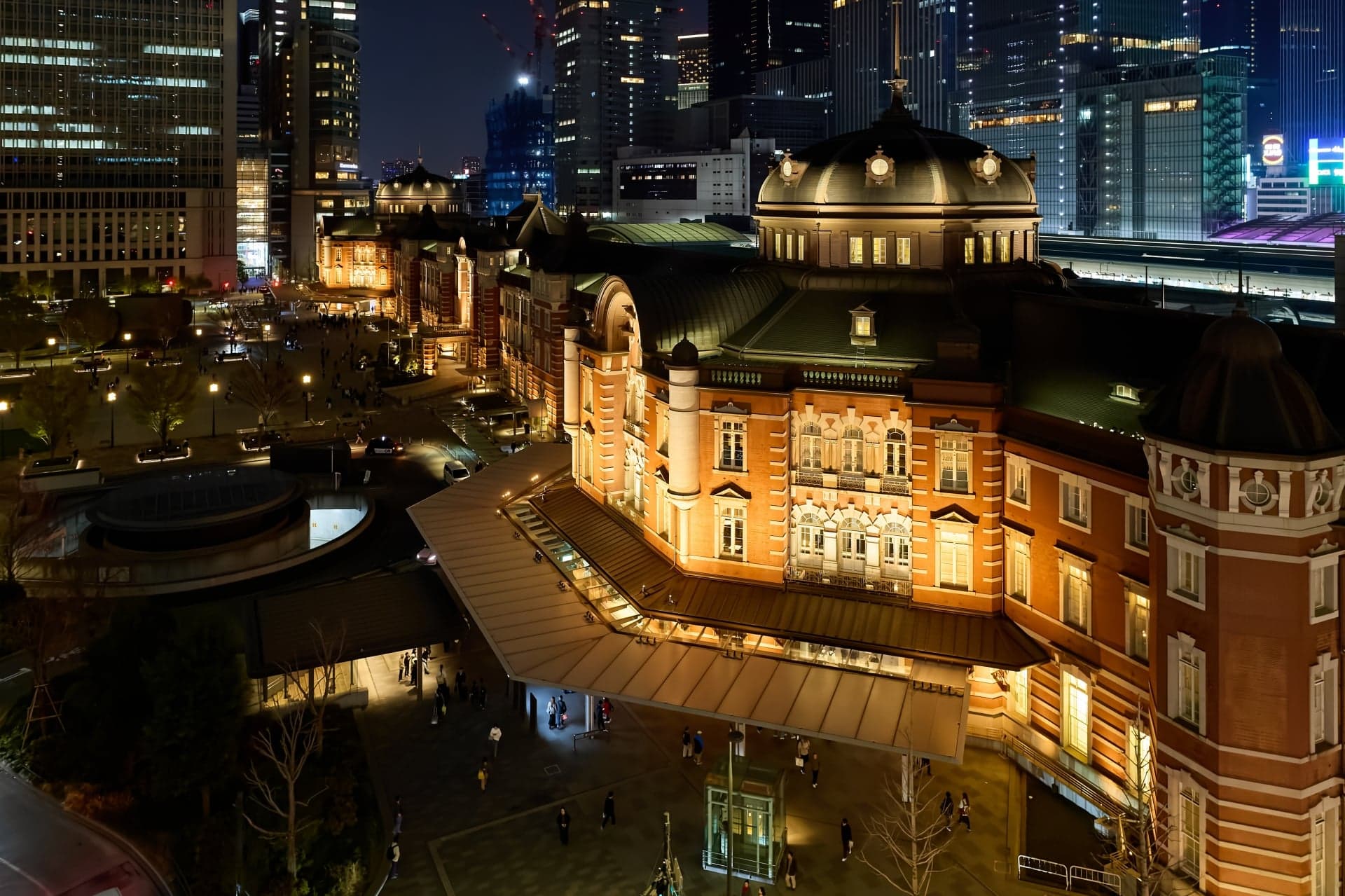 The domes and roof of Tokyo Station seen from above at night, with office towers behind