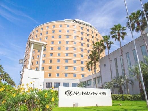 The Maihama View Hotel building behind palm trees and a lawn under a blue sky