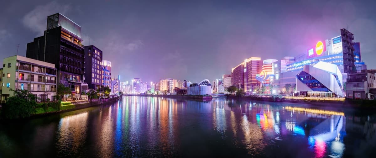Fukuoka's riverside nightlife district at night, its neon lights reflected in the water