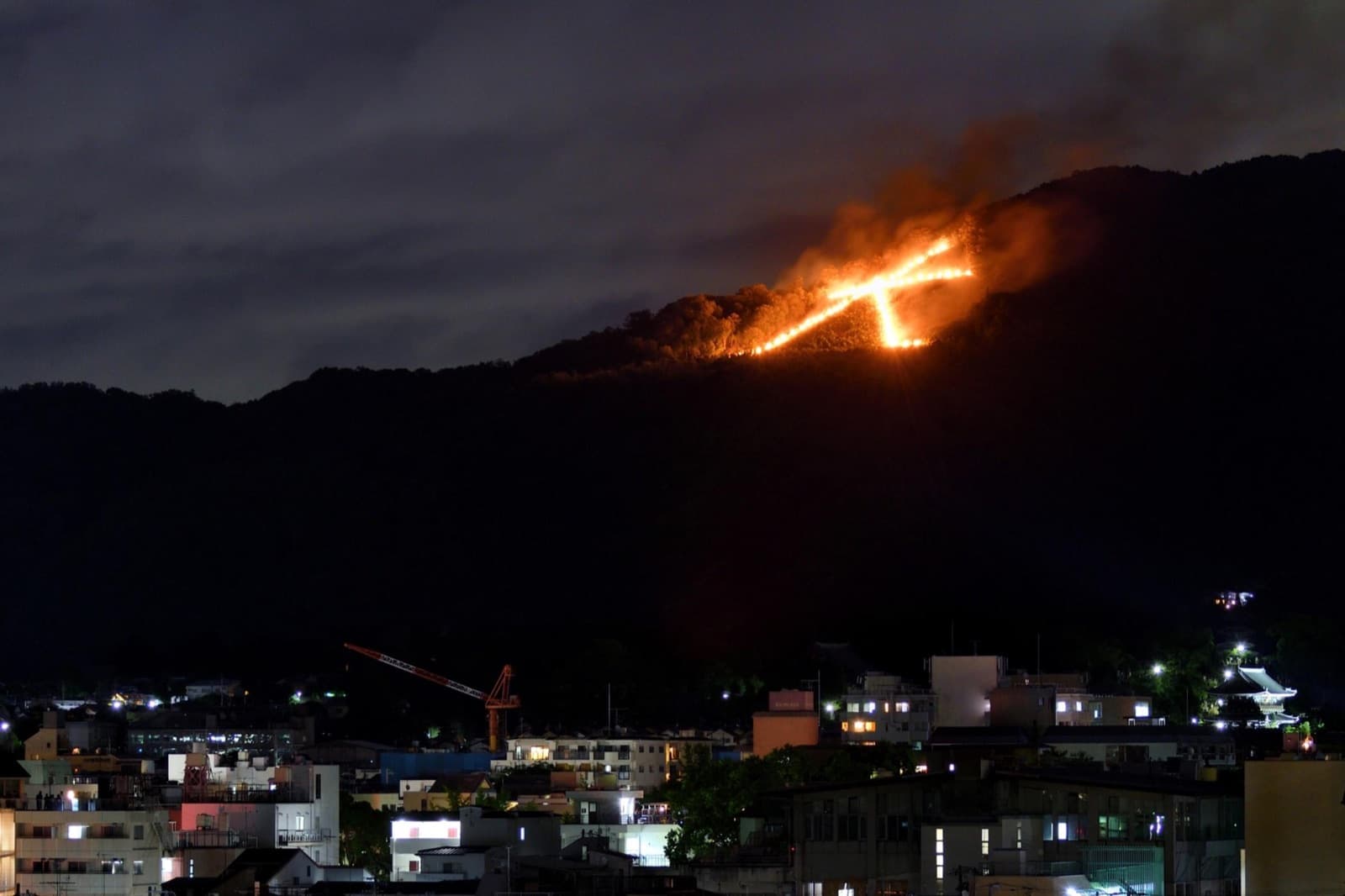 A Kyoto mountainside bonfire glowing over the city at night during Obon