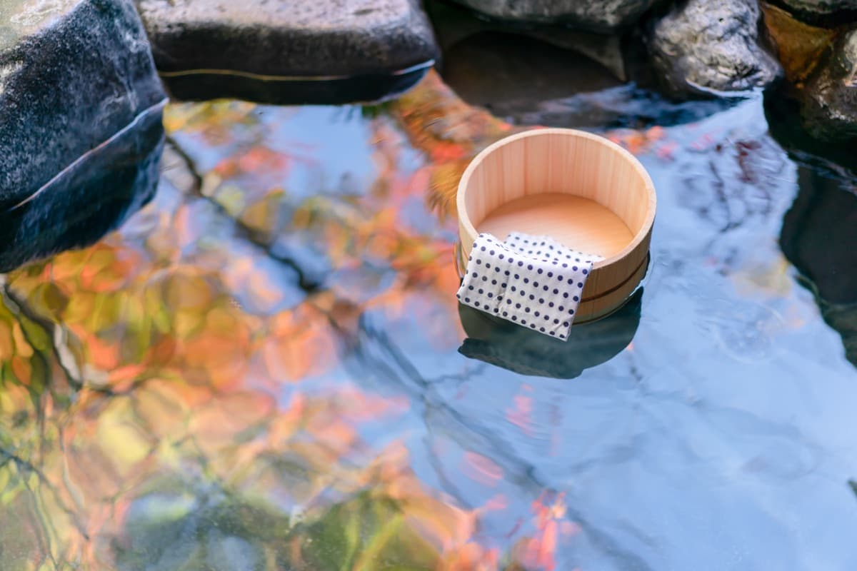 Un cubo de madera y una toalla junto a un baño termal al aire libre en otoño