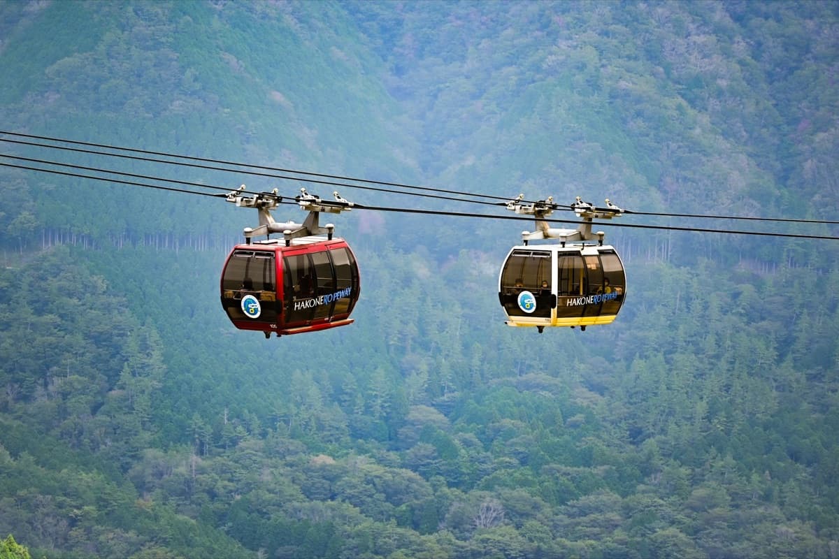 Two Hakone Ropeway gondolas crossing above forested slopes