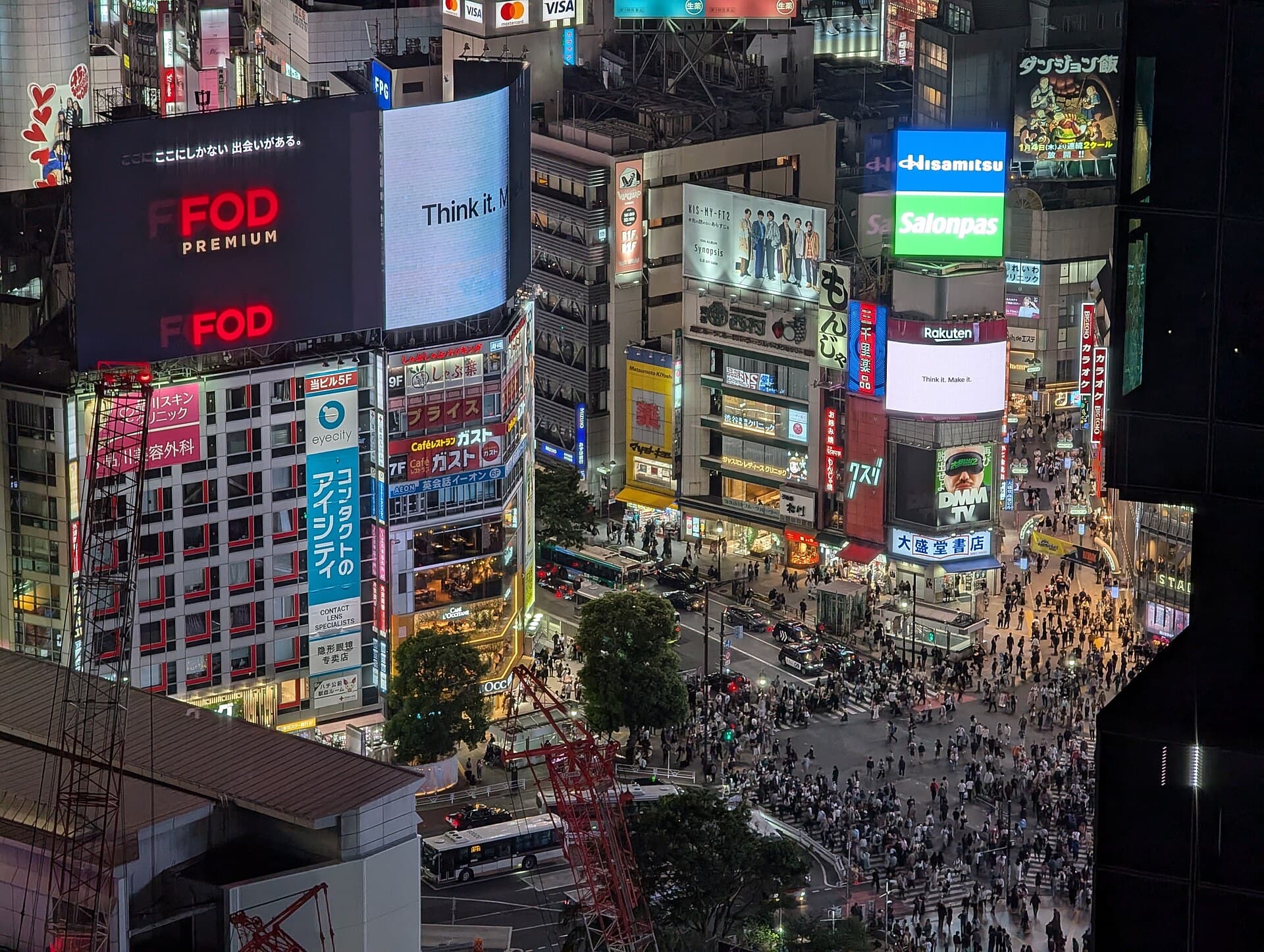 Shibuya scramble crossing at night with crowds crossing safely under bright billboards