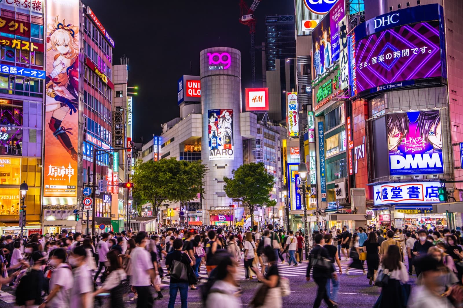 Crowds crossing the Shibuya scramble at night beneath neon signs and the Shibuya 109 tower