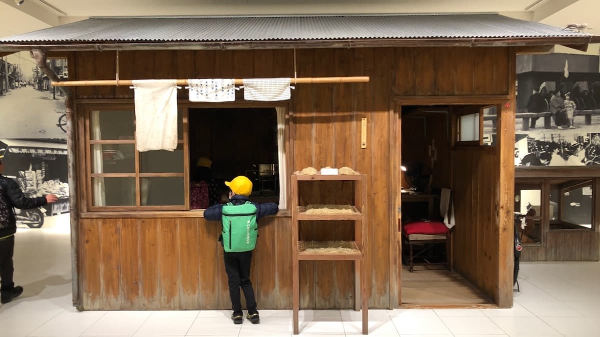 A child looking into a replica of a small wooden backyard shed inside a Cup Noodles Museum