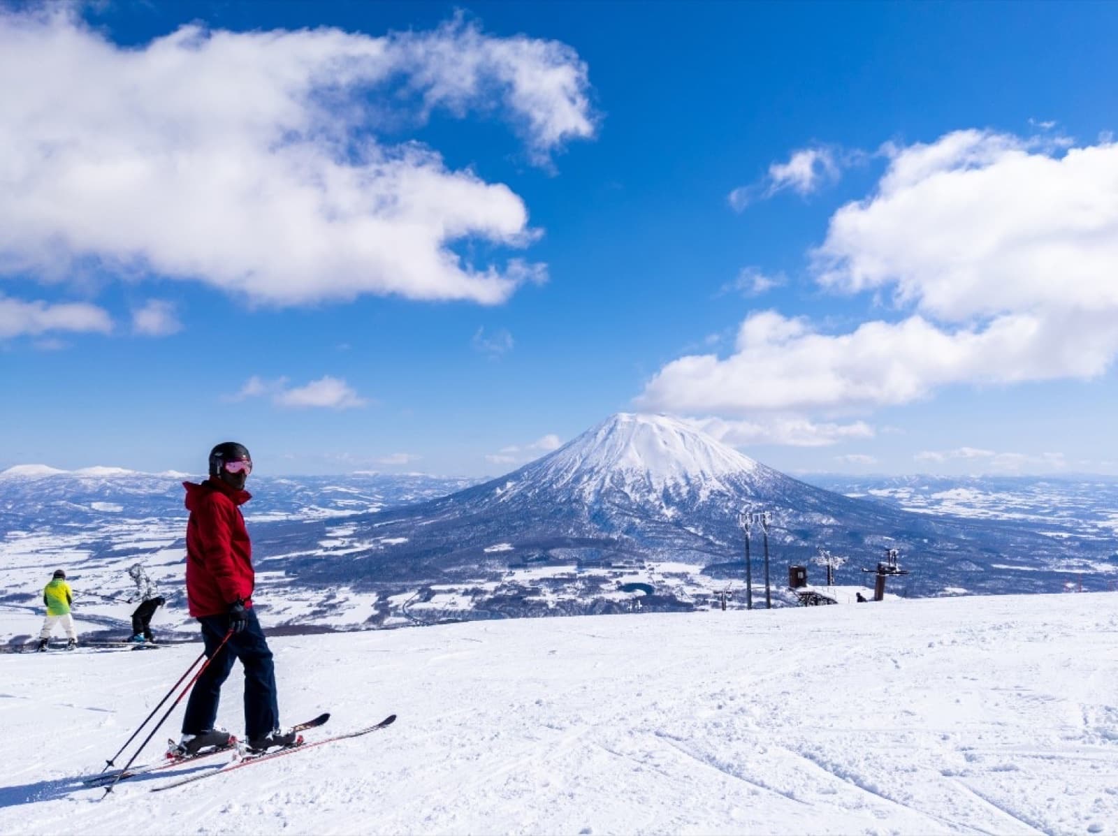 Skieur sur une piste damée à Niseko, avec le mont Yotei et un ciel bleu en arrière-plan