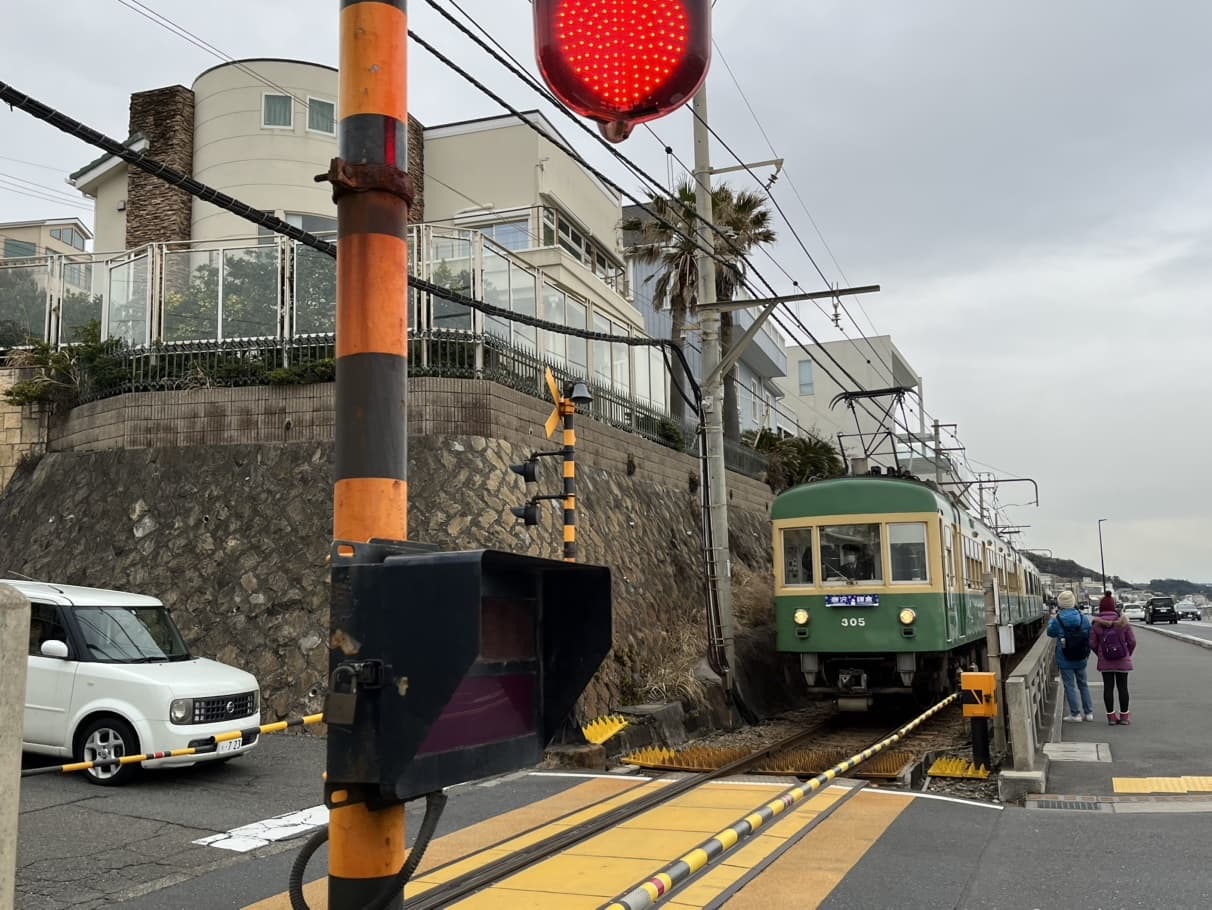 A green-and-cream Enoden local train passing a level crossing in a coastal Kamakura neighbourhood
