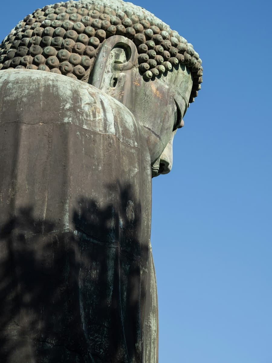 The bronze Great Buddha of Kamakura seen from the side against a blue sky