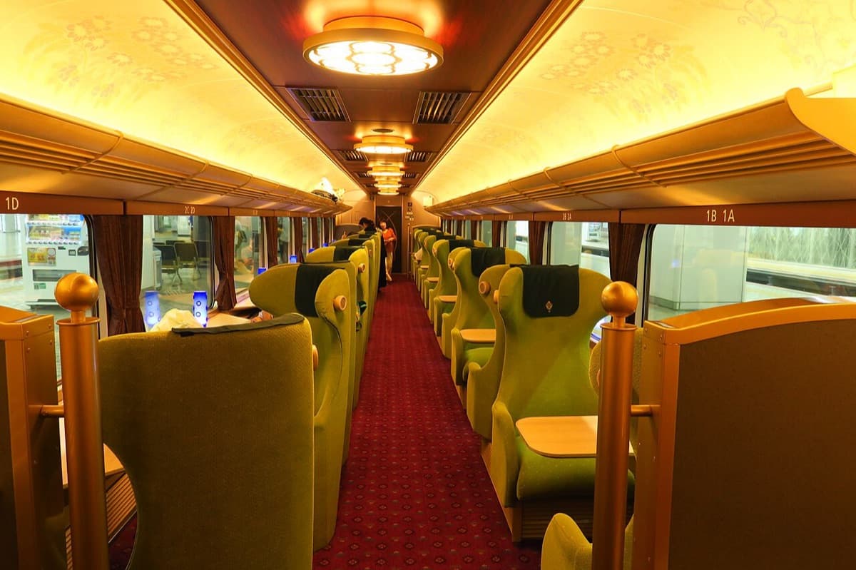 Inside a car of Kintetsu's Aoniyoshi train: green armchairs in pairs facing small tables by the windows, under warm ceiling lights