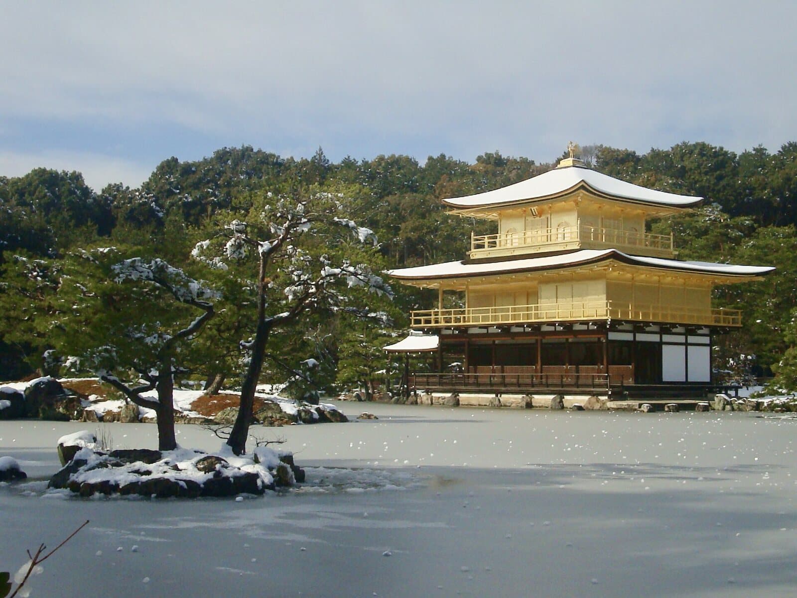 Kinkaku-ji's golden pavilion with snow on its roofs, the pond in front frozen over and snow on the pine-covered islets