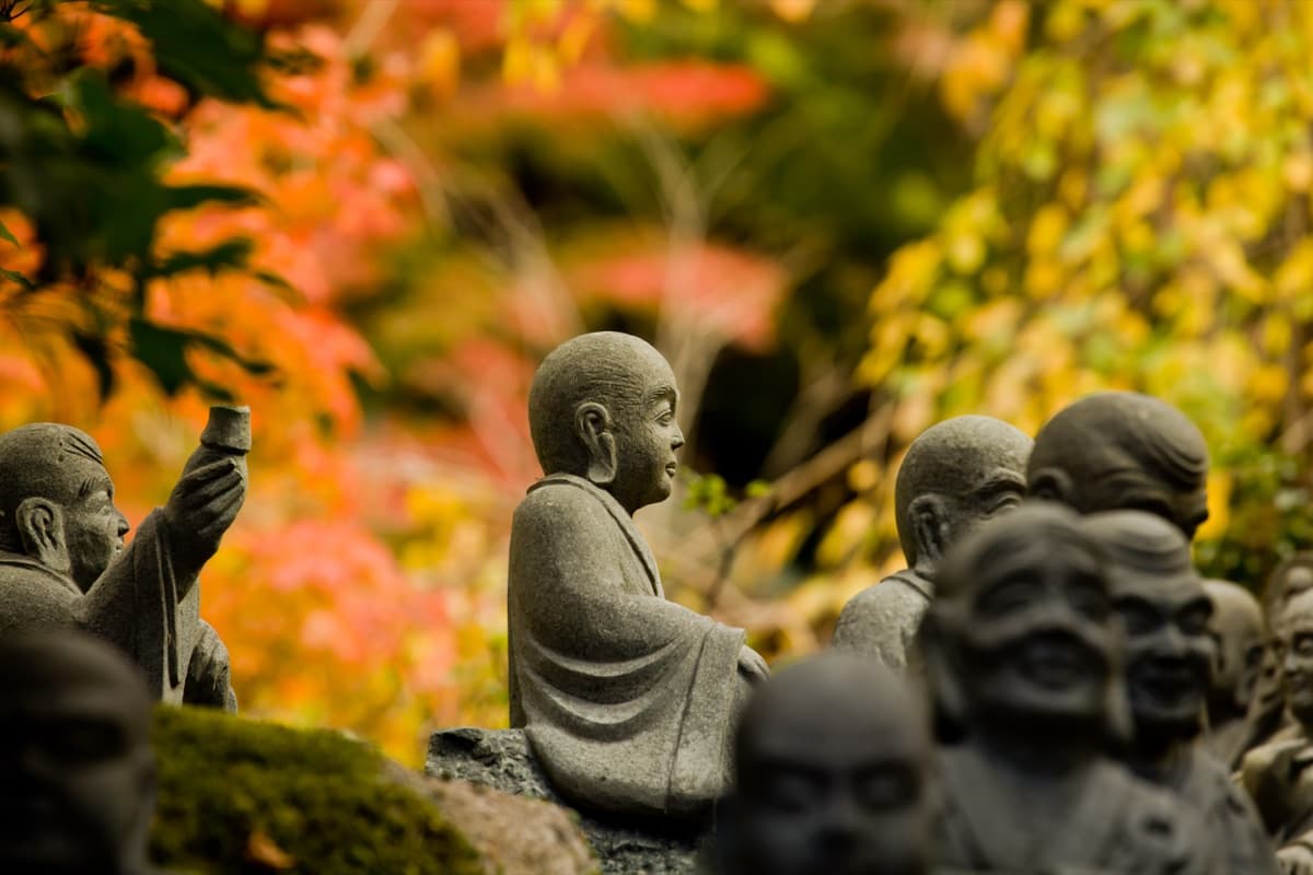 Moss-covered rakan statues among red and gold maples at Daisho-in temple on Miyajima