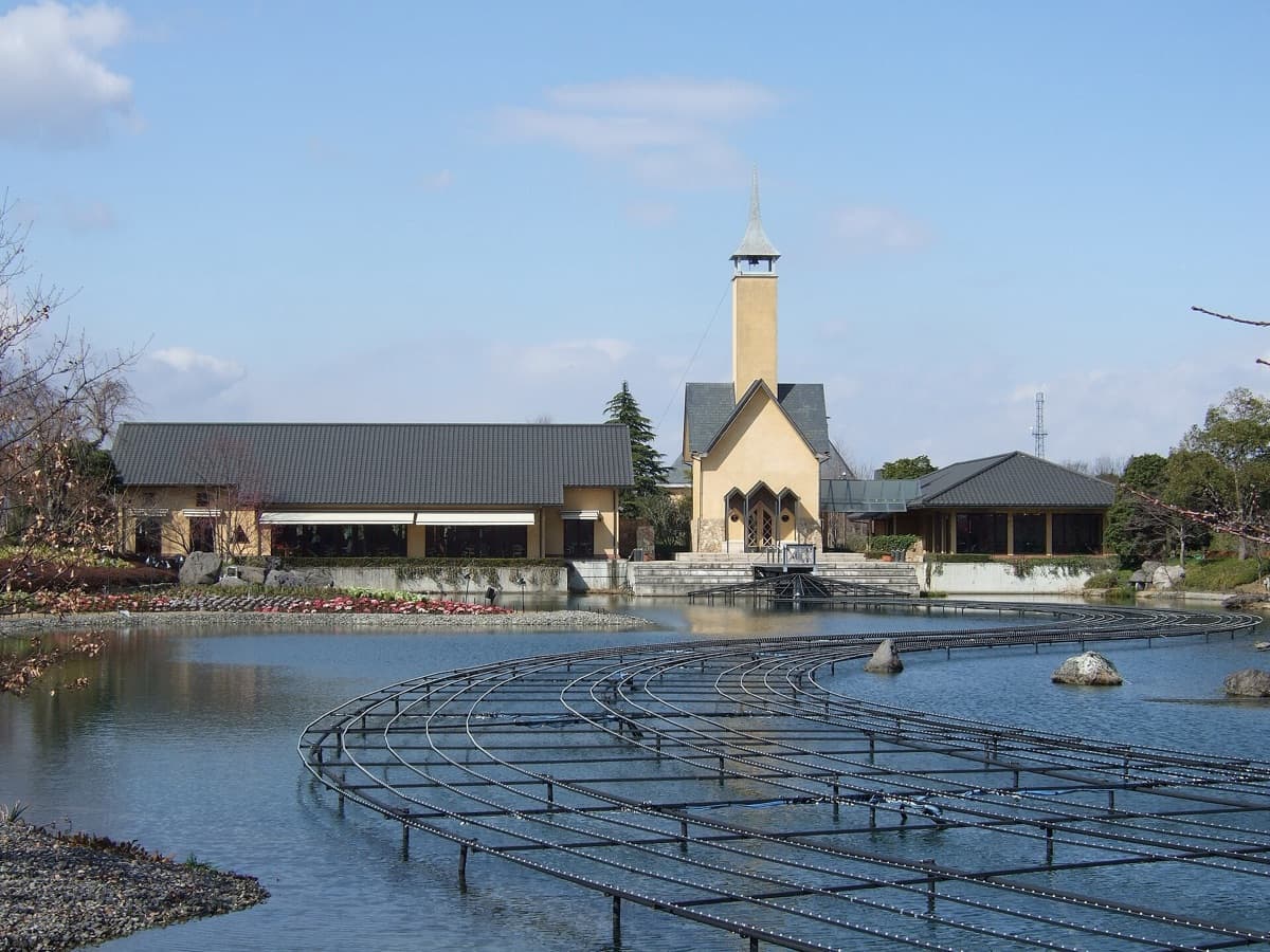 The Nabana no Sato pond by day with a white chapel tower and restaurant buildings on the far bank