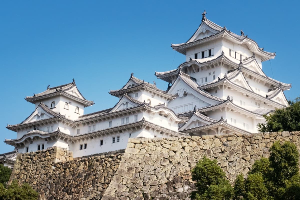 La torre blanca de varios pisos del castillo de Himeji sobre altas murallas de piedra bajo un cielo azul