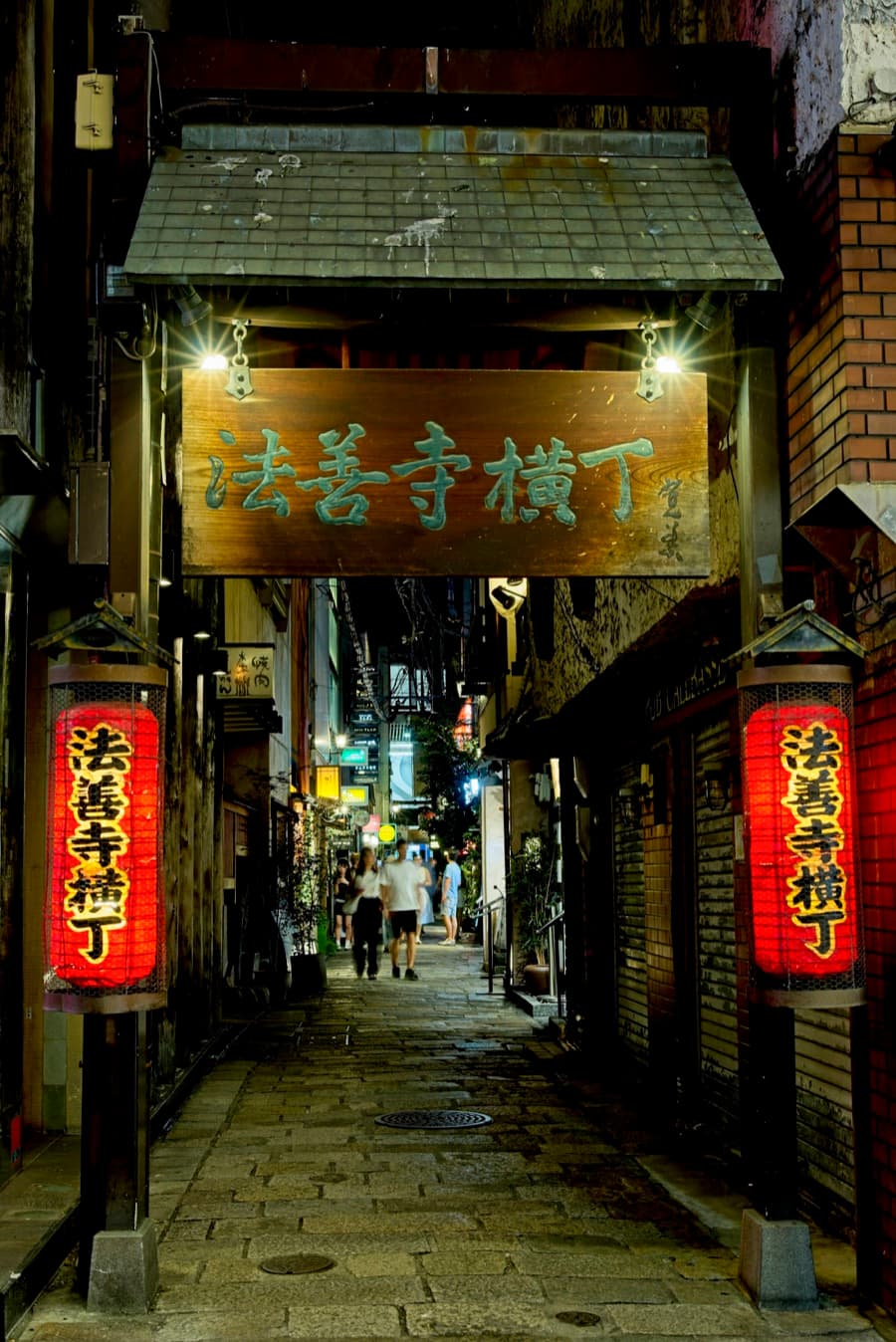 El estrecho callejón empedrado de Hozenji Yokocho de noche, con farolillos rojos y un letrero de madera