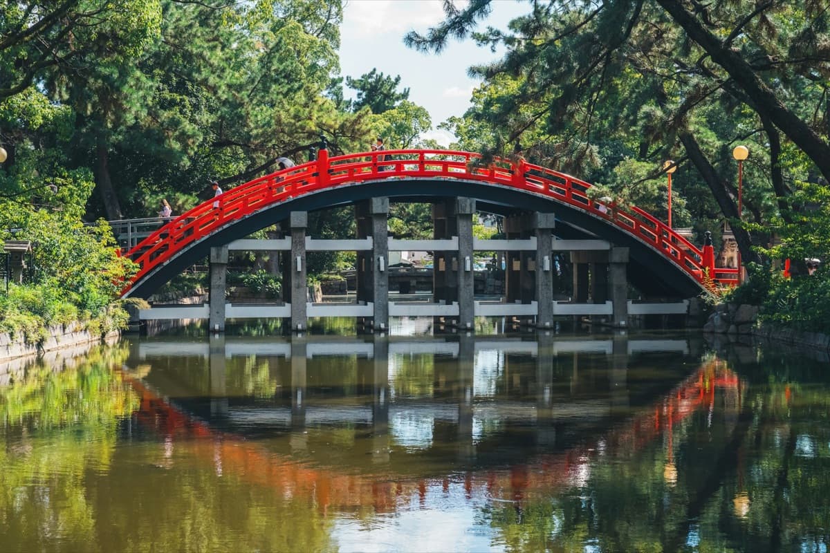 El puente rojo arqueado Sorihashi del santuario Sumiyoshi Taisha reflejado en el estanque entre árboles