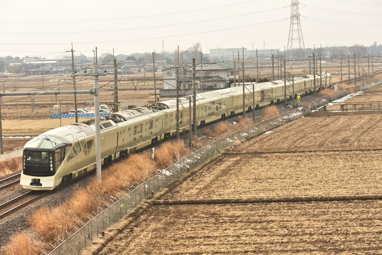The champagne-gold Train Suite Shiki-shima with its sloping glass-fronted observation car running past winter fields