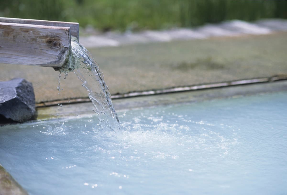 De l’eau thermale laiteuse coule d’un bec en bois dans un bain extérieur