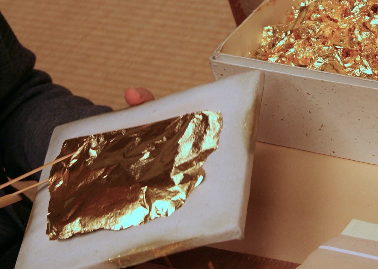 A hand holding a tray with sheets of gold leaf in a Kanazawa workshop