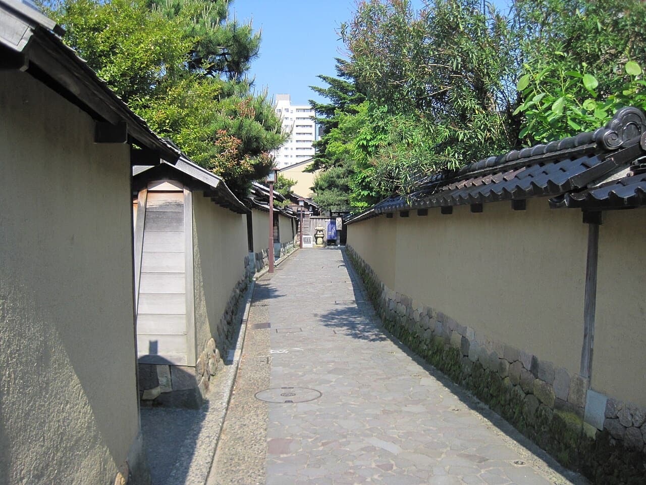 A narrow stone-paved lane between tall earthen walls with tiled caps in the Nagamachi samurai district