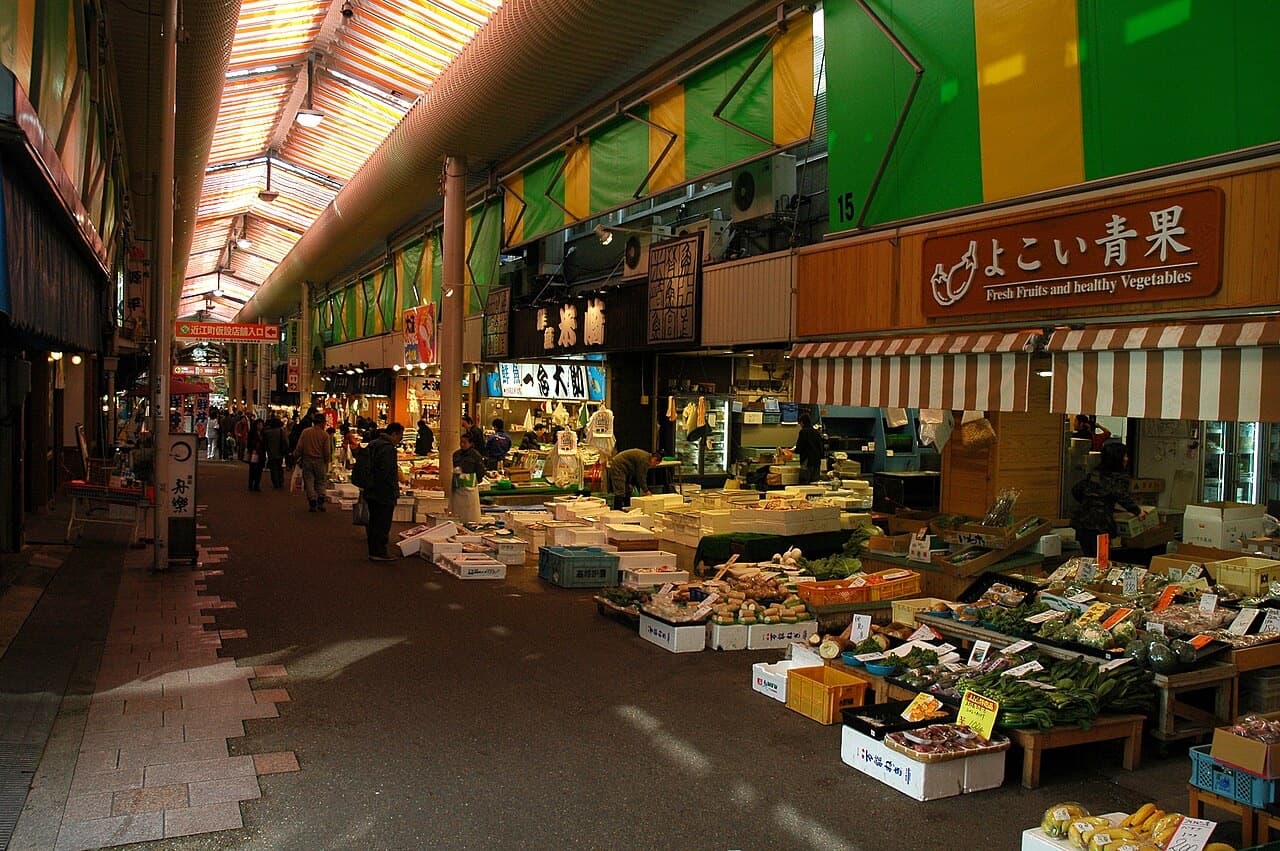 Shoppers walking through the covered lanes of Omicho Market past fresh produce and seafood stalls